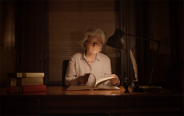 Szenische Darstellung einer Frau die am Schreibtisch sitzt und ein Buch ließt